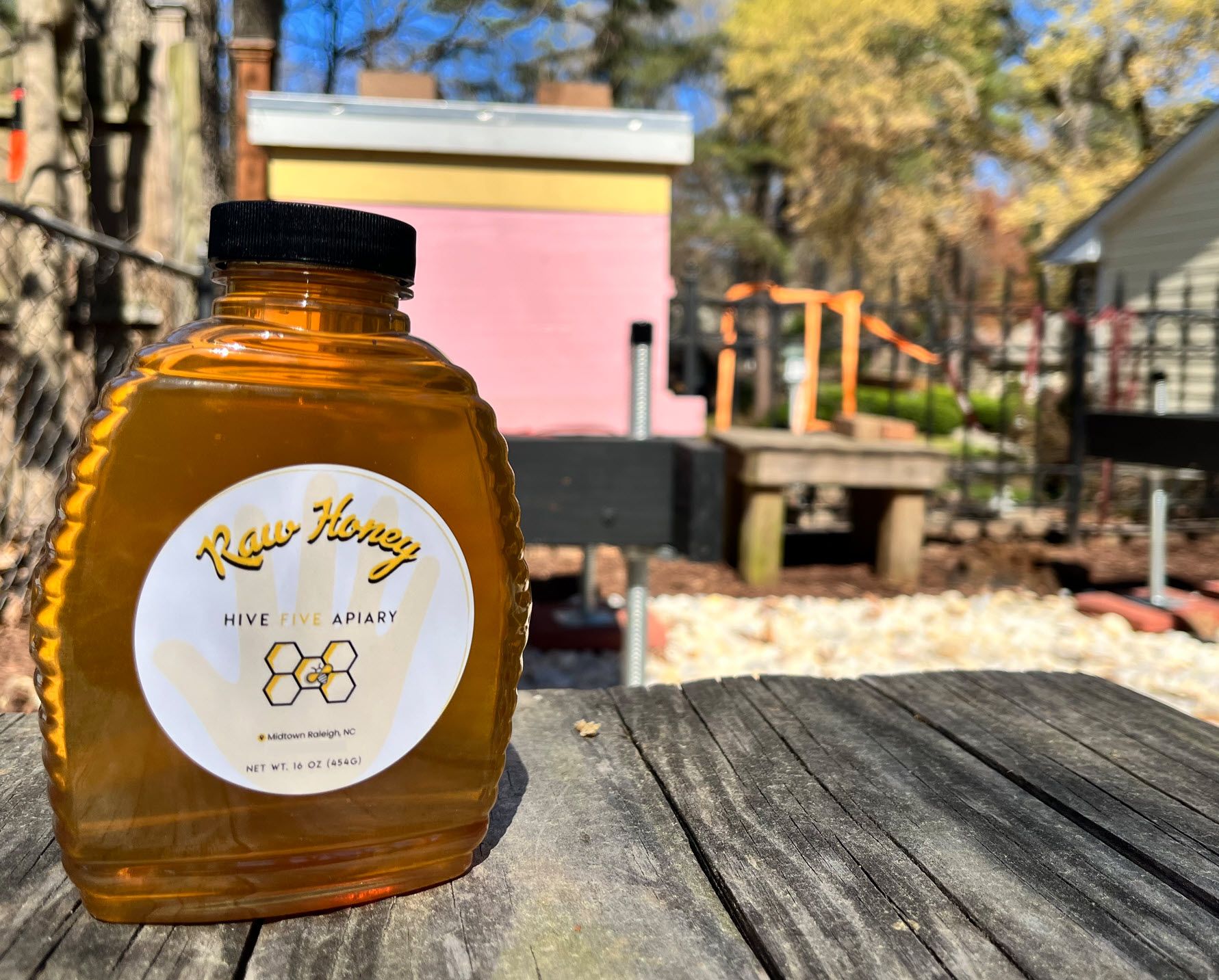 Bottle of Hive Five Apiary raw honey with our hives in the background