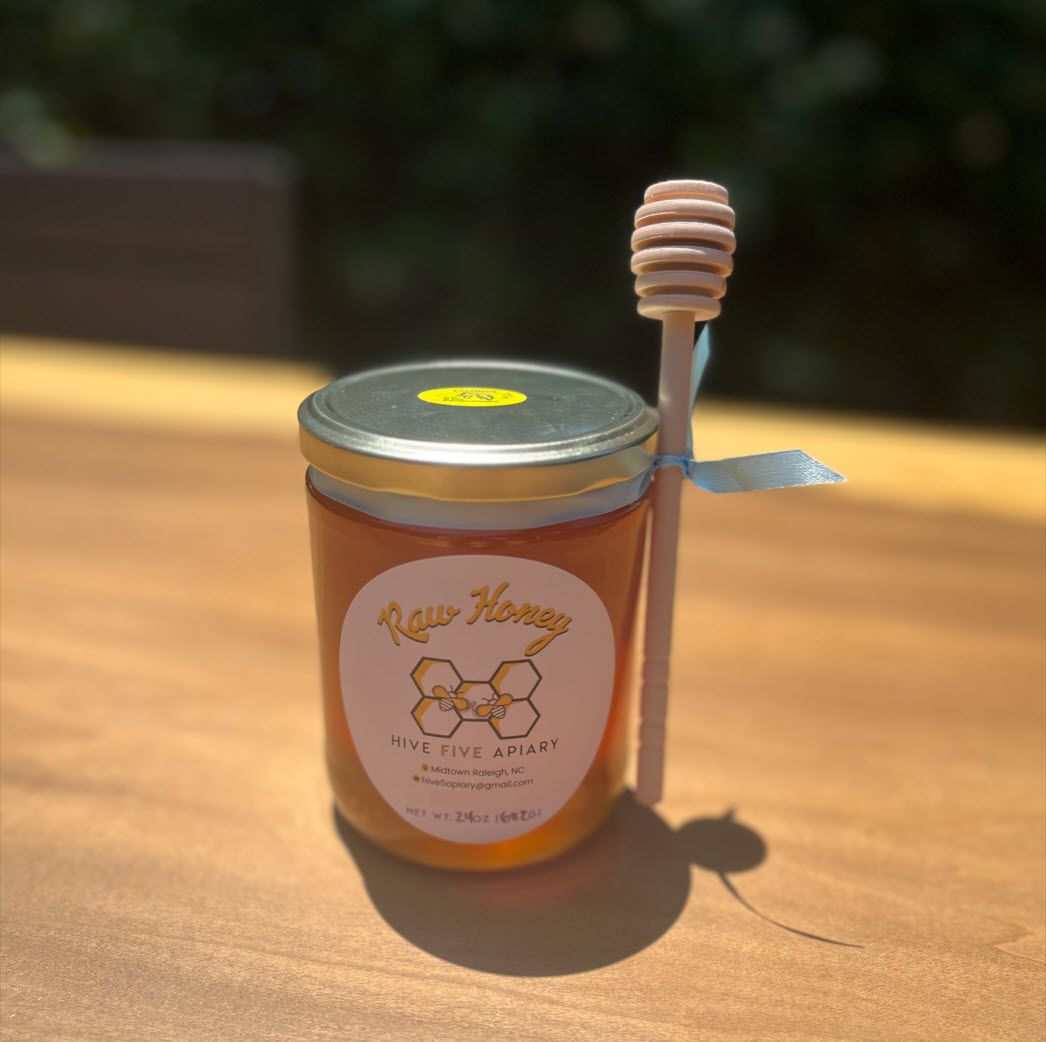 Glass jar of Hive Five Apiary raw honey with a wooden honey dipper